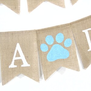 May include: A burlap banner with the words "Paw-ty" in white letters. The banner has a blue paw print in the middle.