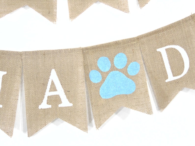 May include: A burlap banner with the words "Paw-ty" in white letters. The banner has a blue paw print in the middle.