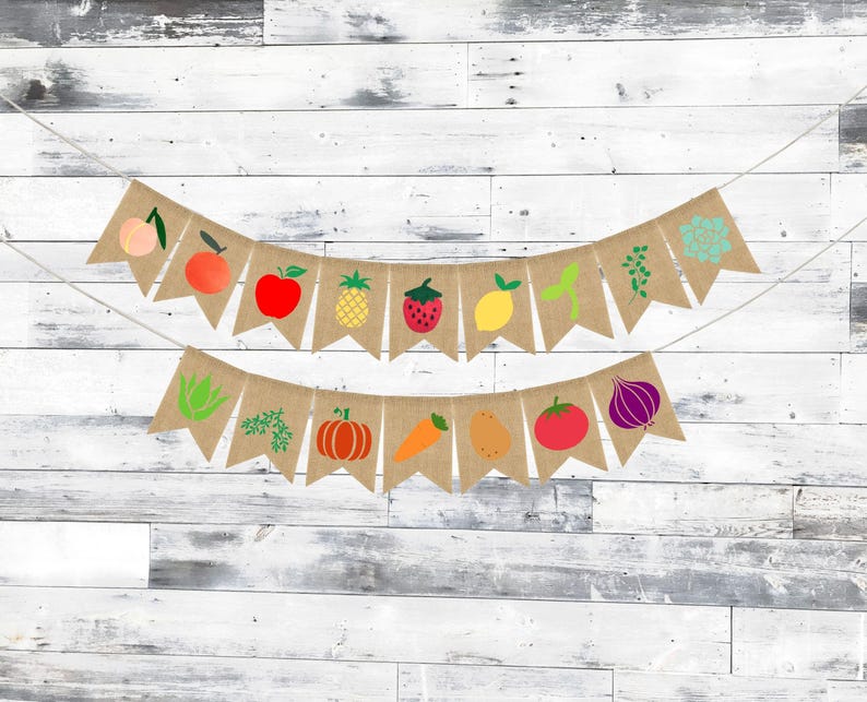 May include: A burlap banner with a string of flags featuring various fruits and vegetables. The flags are decorated with images of a peach, apple, pineapple, strawberry, lemon, carrot, pumpkin, tomato, onion, and a sprig of greenery.