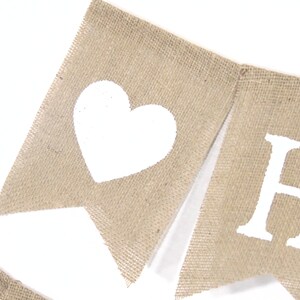 May include: A burlap banner with white painted letters spelling "HOME" and a white heart on the left side.