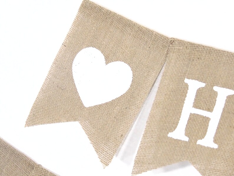 May include: A burlap banner with white painted letters spelling "HOME" and a white heart on the left side.