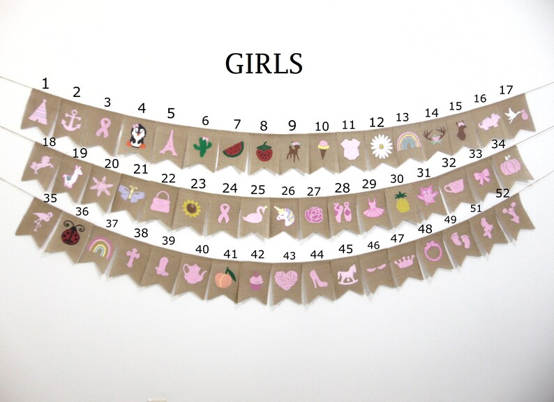 May include: A burlap banner with pink and white illustrations of various girls' themed items, including a unicorn, a flamingo, a crown, a teapot, a cupcake, a ballerina, a pineapple, a rainbow, a ladybug, a butterfly, a flower, a watermelon, a cactus, a Christmas tree, a rocking horse, a pair of ballet shoes, a shoe, a heart, a peach, a pumpkin, a bow, a teacup, a star, a llama, a purse, a sunflower, a ribbon, a cross, a boot, a deer, a bird, and an anchor. The banner is numbered 1 through 52.