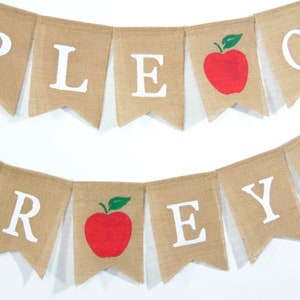 Może przedstawiać: Baner z juty z napisem "Apple-A-Day" białymi literami. Baner ma namalowane czerwone jabłka z zielonymi liśćmi.