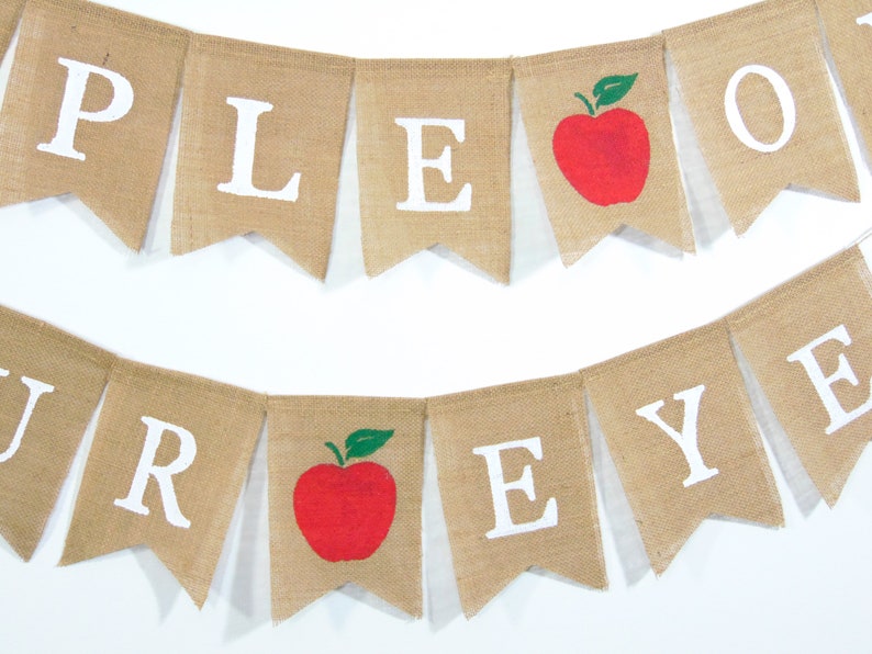 Może przedstawiać: Baner z juty z napisem "Apple-A-Day" białymi literami. Baner ma namalowane czerwone jabłka z zielonymi liśćmi.