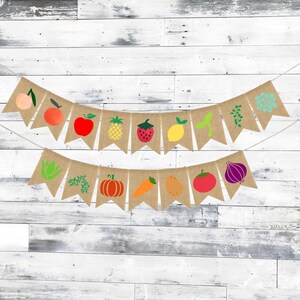 May include: A burlap banner with a string of flags featuring various fruits and vegetables. The flags are decorated with images of a peach, apple, pineapple, strawberry, lemon, carrot, pumpkin, tomato, onion, and a sprig of greenery.