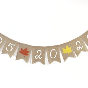 May include: A burlap banner with white numbers and orange and yellow leaf cutouts, spelling out "05 20 22".
