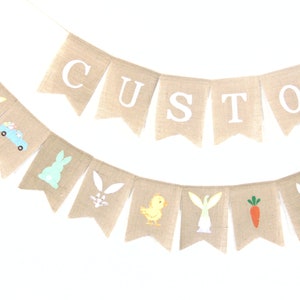 K&ouml;nnte beinhalten: Ein Banner aus Jute mit dem Wort "CUSTOM" in wei&szlig;en Buchstaben. Das Banner ist mit Ostern-Motiven verziert, darunter Hasen, K&uuml;ken, Karotten und ein Osterei.