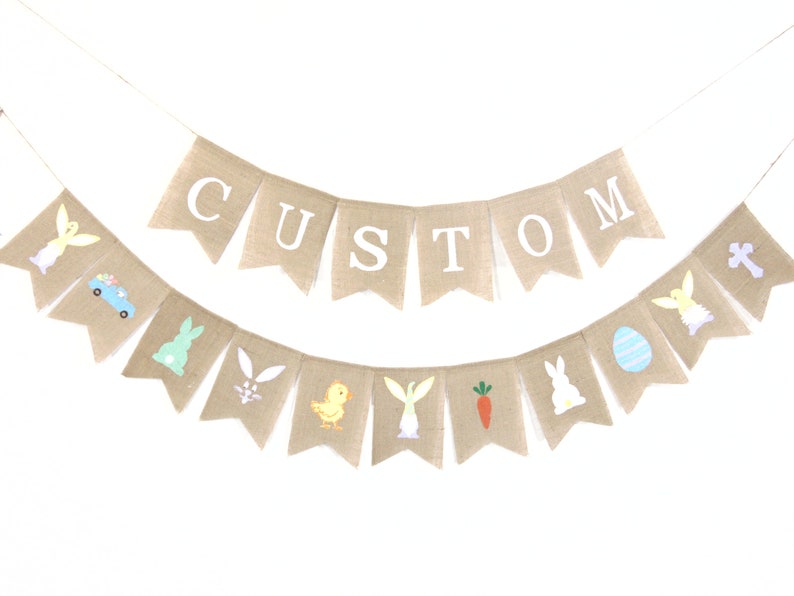 K&ouml;nnte beinhalten: Ein Banner aus Jute mit dem Wort "CUSTOM" in wei&szlig;en Buchstaben. Das Banner ist mit Ostern-Motiven verziert, darunter Hasen, K&uuml;ken, Eier und Karotten.