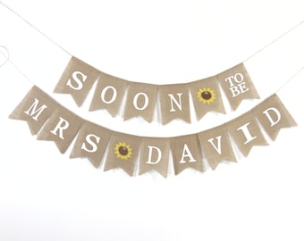May include: A burlap banner with the text "Soon to be Mrs. David" in white letters. The banner has sunflowers on each side of the text.