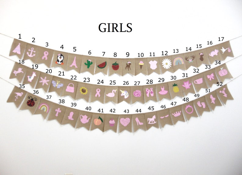 May include: A burlap banner with pink and white illustrations of various girls' themed items, including a unicorn, a flamingo, a crown, a teapot, a cupcake, a ballerina, a pineapple, a rainbow, a ladybug, a butterfly, a sunflower, a watermelon, a cactus, a Christmas tree, a rocking horse, a pair of ballet shoes, a daisy, a pumpkin, a bow, a teacup, a star, a llama, a purse, a pink ribbon, a heart, a shoe, a peach, a cross, a boot, an anchor, a penguin, a deer, a bird, and a pair of footprints. The banner is labeled "GIRLS" and numbered 1 through 52.