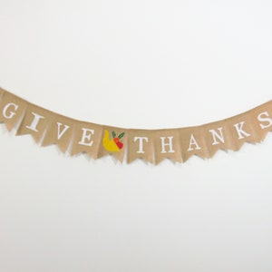 May include: A burlap banner with the words "GIVE THANKS" in white letters. The banner has a yellow and red cornucopia design on each end.