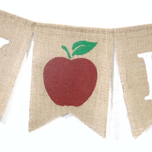 Puede incluir: Una pancarta de arpillera con las palabras "Happy" y "Fall" en letras blancas. La bandera del medio presenta una manzana roja con una hoja verde.