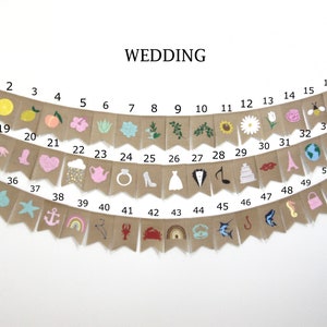 Puede incluir: Una pancarta de arpillera con 52 banderas, cada una con un dise&ntilde;o ilustrado diferente. La pancarta est&aacute; decorada con varios s&iacute;mbolos relacionados con la boda, incluyendo un cactus, un coraz&oacute;n, un anillo, un vestido, un esmoquin, una nota musical, un pastel, una Torre Eiffel, un globo terr&aacute;queo y una copa de vino. La pancarta est&aacute; etiquetada con los n&uacute;meros del 1 al 52.