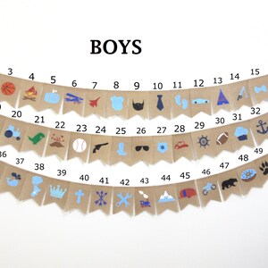 May include: A burlap banner with blue and white illustrations of various boy-themed icons, including a baseball, a sailboat, a rocket, a tie, a crown, and a wrench. The banner is labeled "BOYS" and numbered 1 through 52.