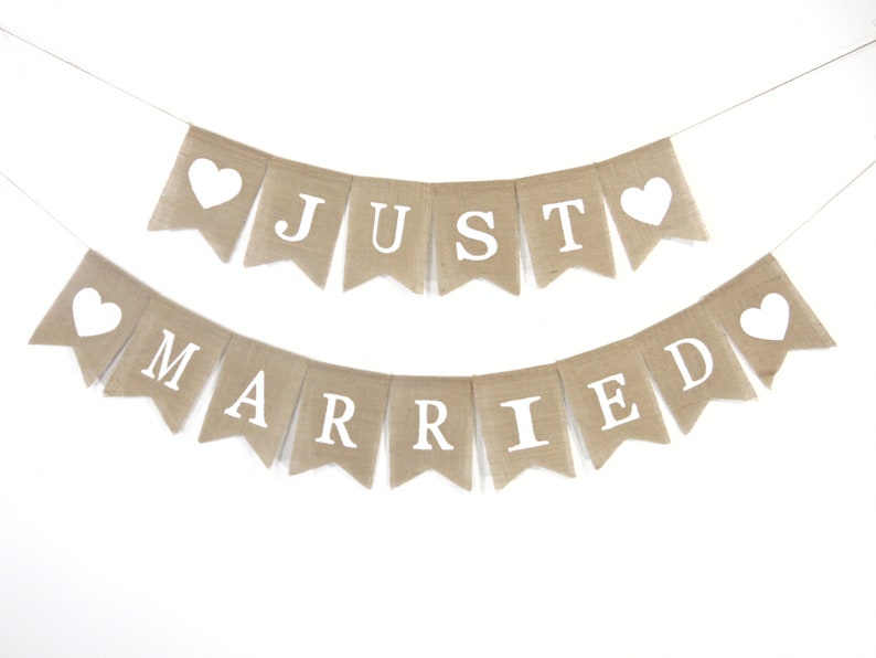 Puede incluir: Una pancarta de arpillera con las palabras "Just Married" en letras blancas. La pancarta est&aacute; decorada con corazones blancos.