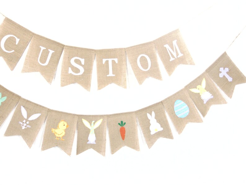 K&ouml;nnte beinhalten: Ein Banner aus Jute mit dem Wort "CUSTOM" in wei&szlig;en Buchstaben. Ein zweites Jutebanner zeigt Bilder zum Thema Ostern, darunter Hasen, K&uuml;ken, Karotten und Eier.