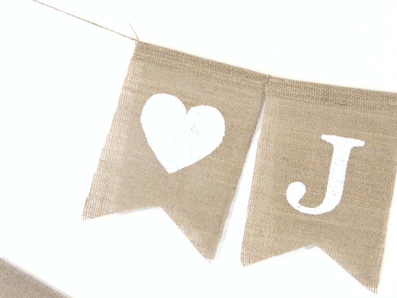 Puede incluir: Una pancarta de arpillera con corazones pintados de blanco y la letra J. La pancarta est&aacute; atada con una cuerda.