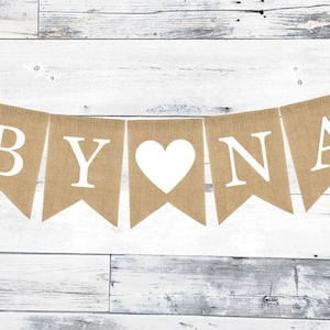 May include: A burlap banner with the words "Baby" in white letters, a white heart, and the word "Nana" in white letters.
