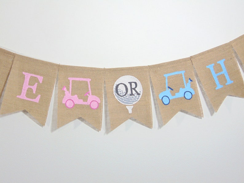 May include: A burlap banner with the words "It's a Girl or Boy" in pink and blue. The banner has a pink golf cart, a golf ball, and a blue golf cart.