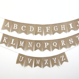 May include: A burlap banner with the alphabet in white letters. The banner is strung up on a white wall.