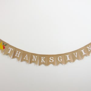 May include: A burlap banner with the words "Happy Thanksgiving" in white letters. The banner has a small turkey illustration with red, yellow, and green accents.