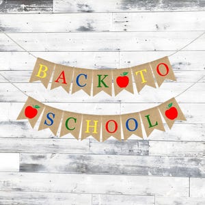 May include: Two burlap banners with the words "BACK TO SCHOOL" in colorful letters and red apple illustrations. The banners are suspended by a white string against a white and gray wooden background. Perfect for classroom decor.