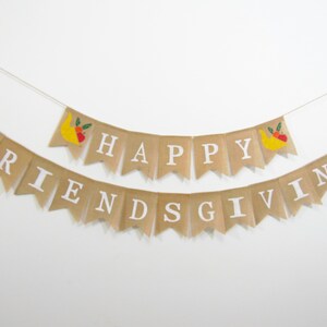 May include: A burlap banner with the words "Happy Friendsgiving" in white letters. The banner is decorated with small, embroidered images of cornucopias filled with fruit.