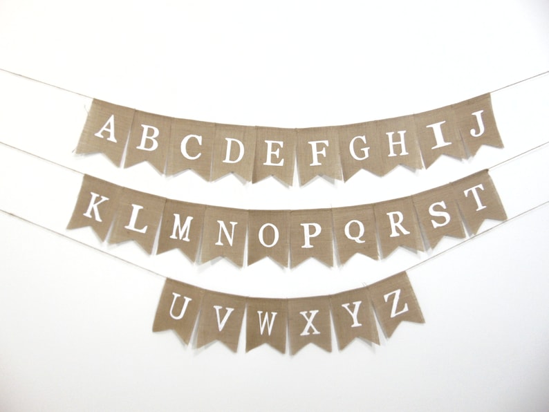 May include: A burlap banner with the alphabet in white letters. The banner is strung up on a white wall.