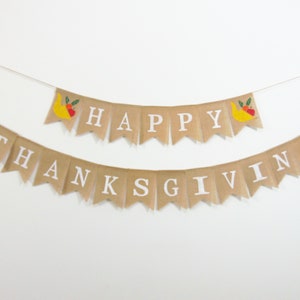 May include: A burlap banner with the words "Happy Thanksgiving" in white letters. The banner is decorated with small, colourful illustrations of fruit.