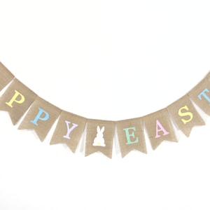 May include: A burlap banner with the words "Happy Easter" in pastel colors. The banner has a white bunny silhouette in the middle.