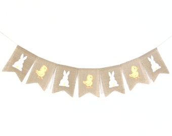 May include: A burlap banner with alternating images of yellow chicks and white bunnies. The banner is strung with white twine and has a scalloped edge.
