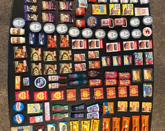 May include: A collection of miniature food items, including candy bars, cereal boxes, and snack packs. The items are arranged on a black surface and include brands like Reese's, Heath, and Dum Dums.