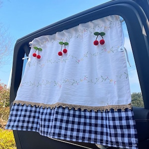Puede incluir: Sombra para ventana de coche a cuadros blancos y azules con un borde de encaje blanco y diseños de cerezas bordados.