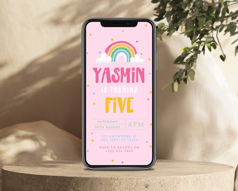 May include: A pink smartphone screen displaying a birthday invitation for Yasmin's fifth birthday. The invitation features a rainbow with stars and a cloud. The text reads "Yasmin is turning Five" with the date and time of the party below.