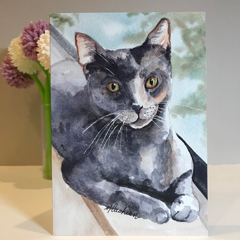 May include: Watercolor painting of a gray and white cat with yellow eyes. The cat is lying down and looking at the viewer. The background is a light blue and green watercolor wash.