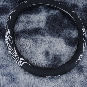 May include: Black leather steering wheel cover with a white embroidered floral design.