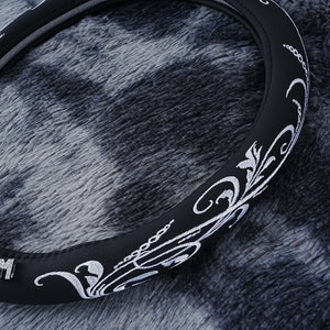 May include: Black leather steering wheel cover with a white embroidered floral design.