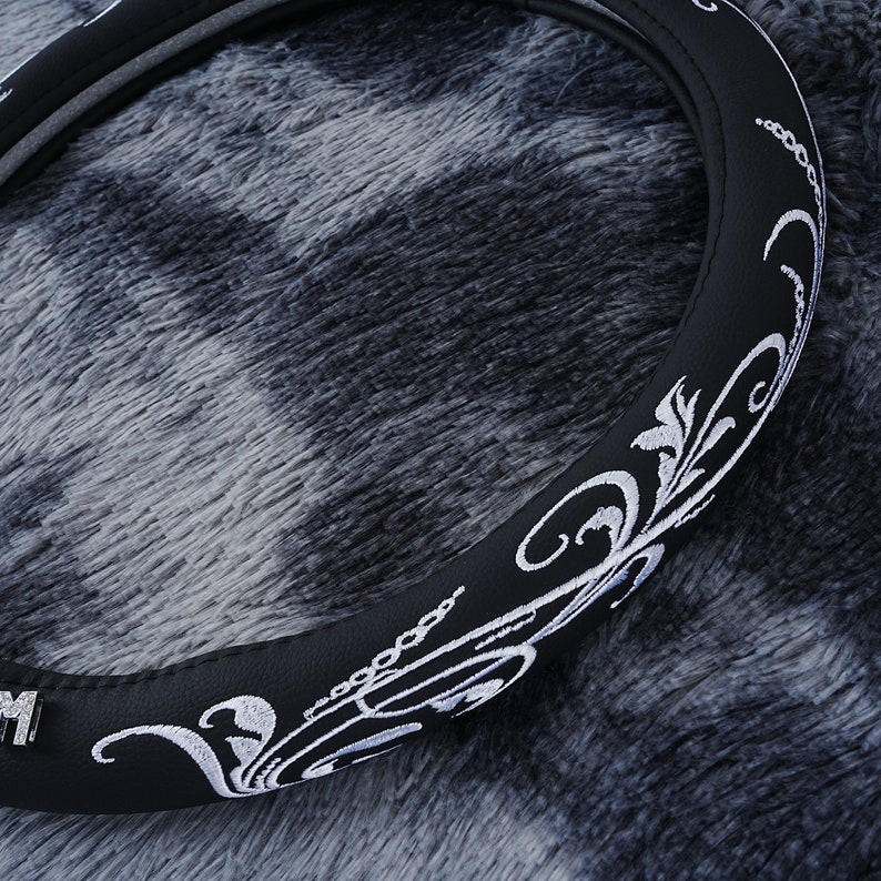 May include: Black leather steering wheel cover with a white embroidered floral design.