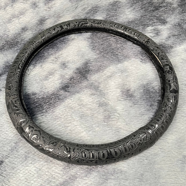 Peut inclure: Housse de volant en cuir noir avec un motif floral en relief.