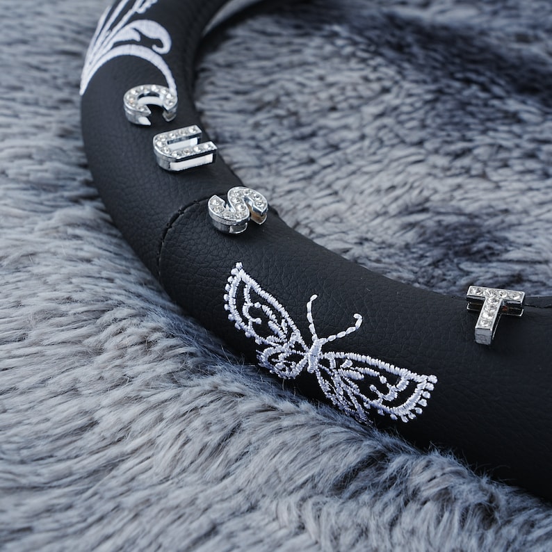 May include: Black leather steering wheel cover with white embroidery of a butterfly and the word "CUTE" with rhinestones.