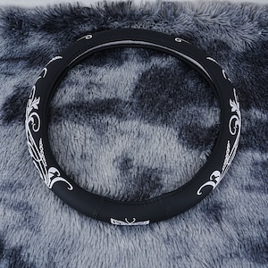 May include: Black leather steering wheel cover with a white floral design. The cover has a butterfly design in the center.