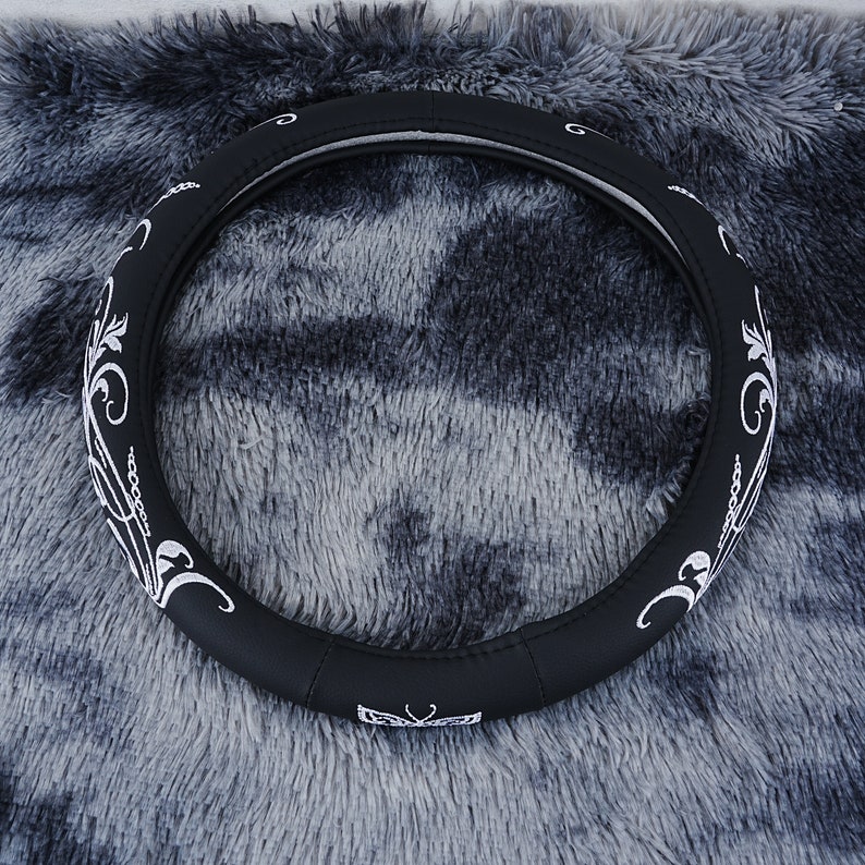 May include: Black leather steering wheel cover with a white floral design. The cover has a butterfly design in the center.