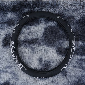 May include: Black leather steering wheel cover with a white floral design.