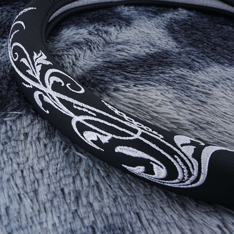 May include: Black steering wheel cover with a white embroidered floral design.
