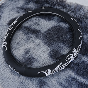 May include: Black leather steering wheel cover with a white floral design.