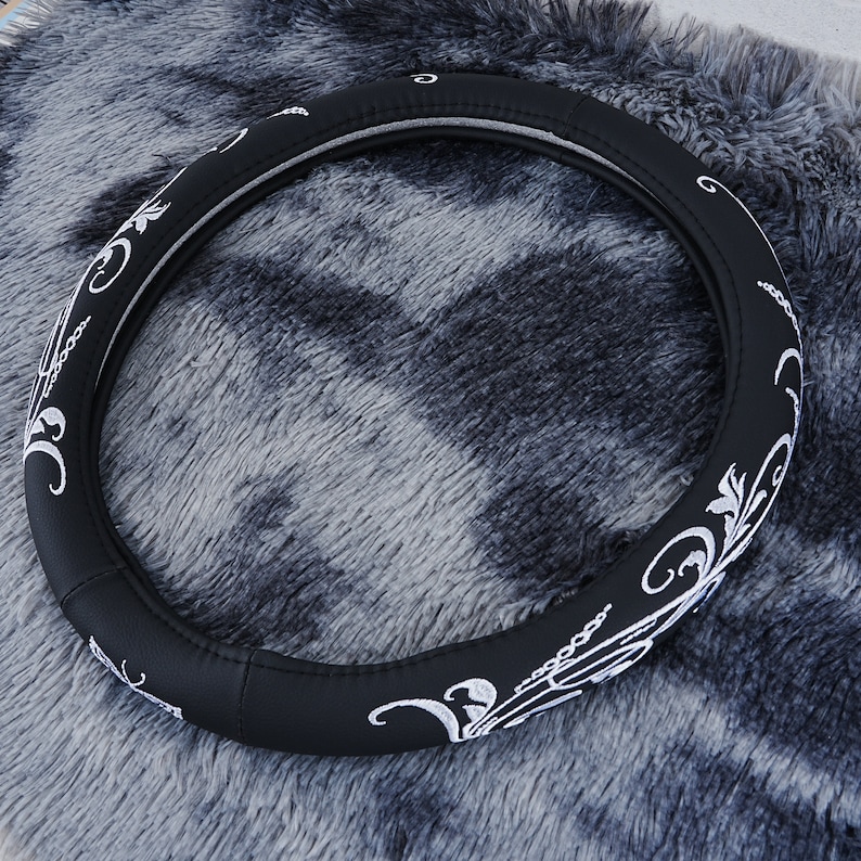 May include: Black leather steering wheel cover with a white floral design.