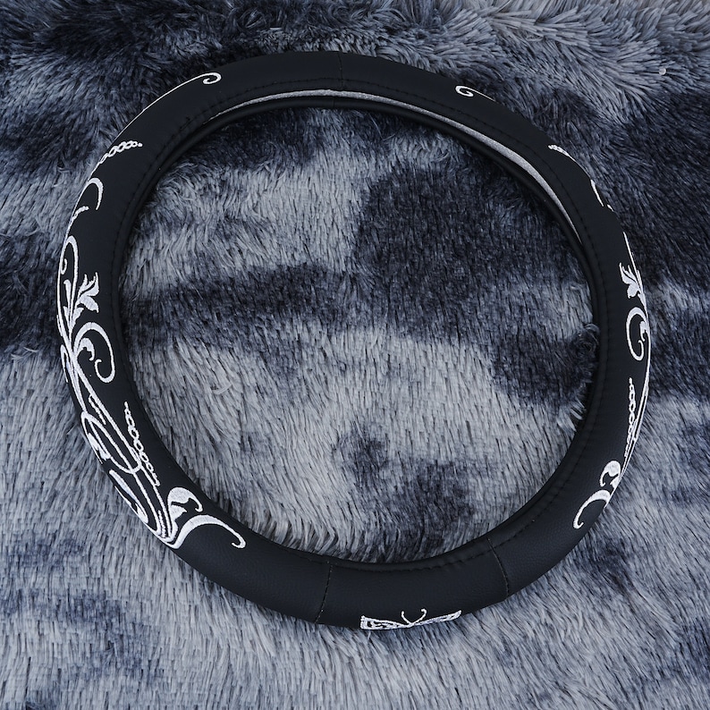 May include: Black leather steering wheel cover with a white embroidered floral design.