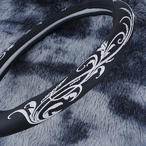 May include: Black leather steering wheel cover with a white embroidered floral design.