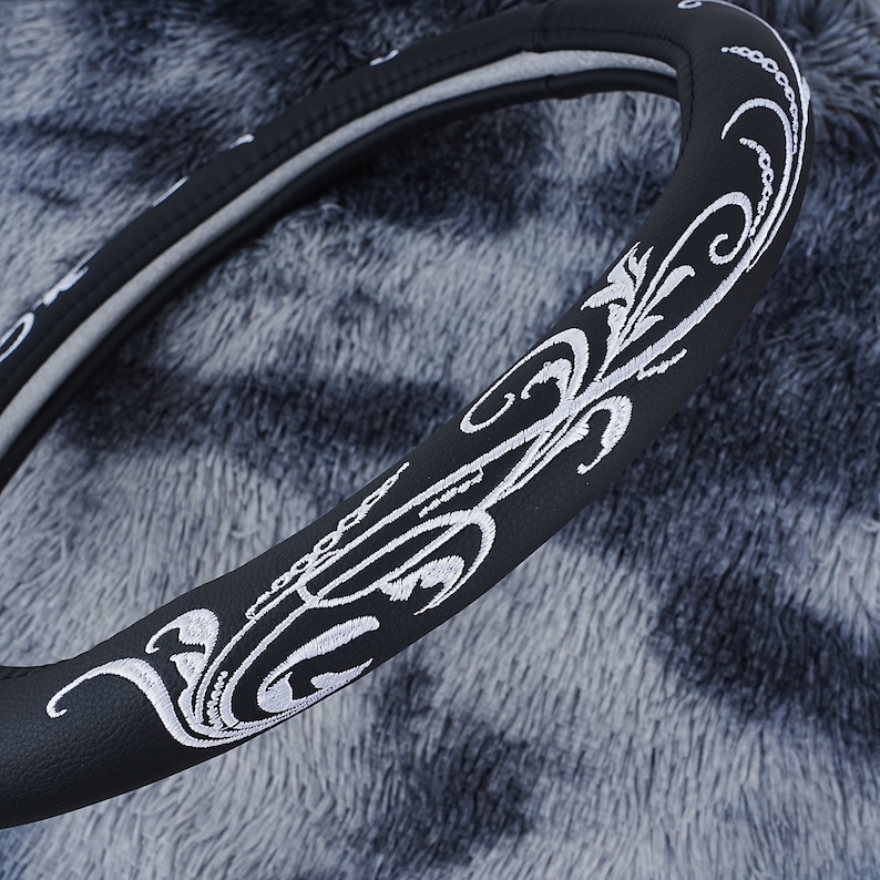 May include: Black leather steering wheel cover with a white embroidered floral design.