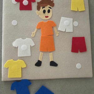 May include: A felt board with a cartoon figure and various felt clothing items. The figure is wearing an orange shirt and shorts. There are red, white, yellow, and blue shirts and shorts. White felt circles are also included.
